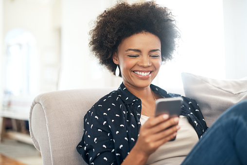 Image of a woman smiling and looking at her phone after knowing her dental care cost is affordable, at Stephen L Ruchlin DDS in Rochester, NY.