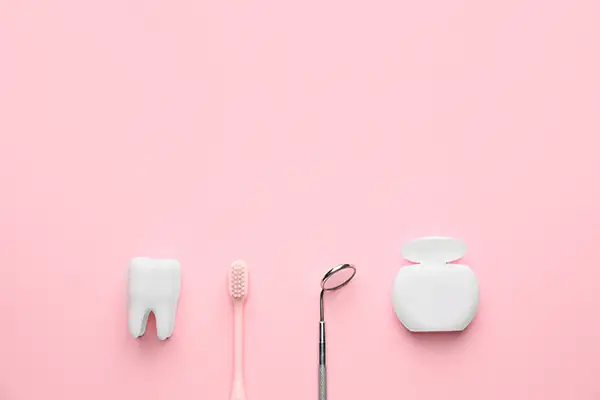 Materials used in a routine dental cleaning procedure, including two plastic containers of dental floss, a toothbrush, and a mirror.