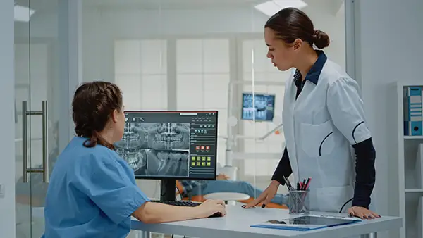 Two dental professionals reviewing detailed full-mouth dental X-rays on a computer screen in a modern clinic.